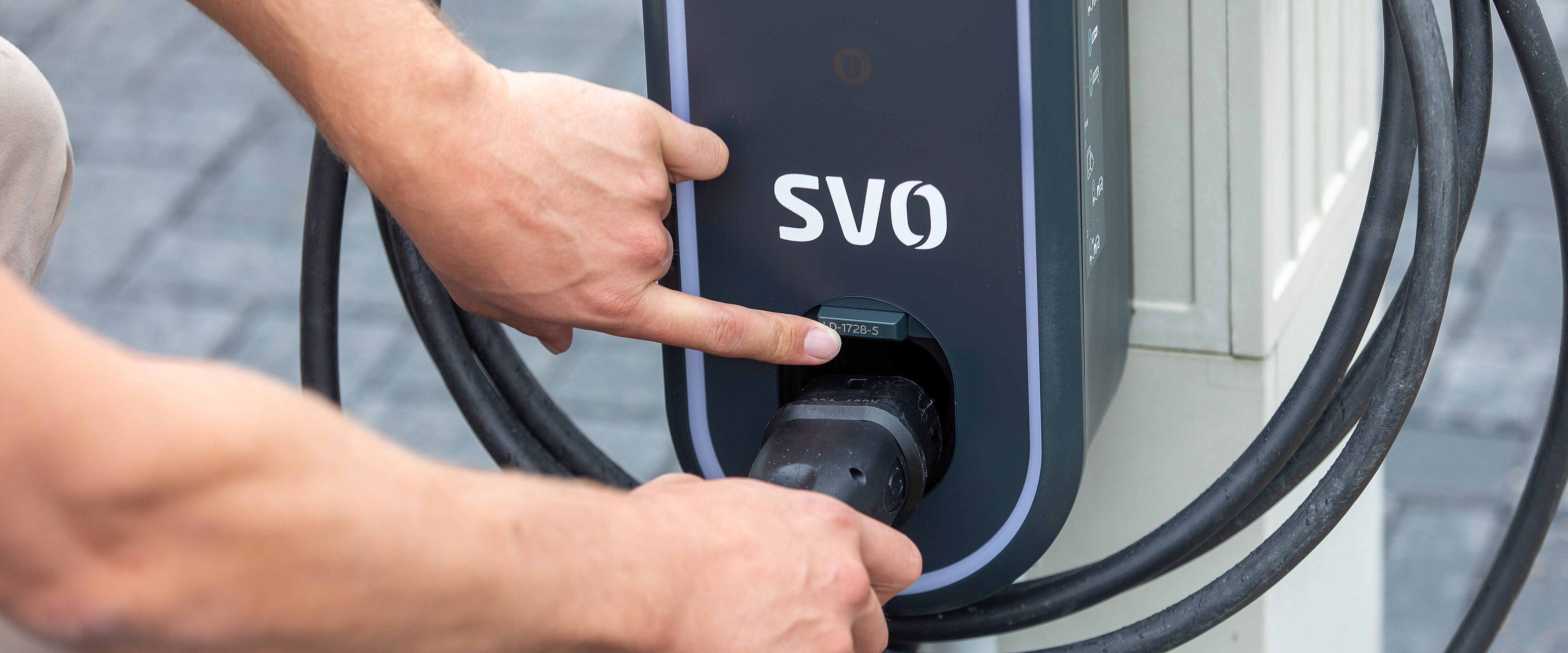 Foto zeigt die Hand einer Person, die einen Ladestecker in die Buchse eines Elektroautos steckt. 